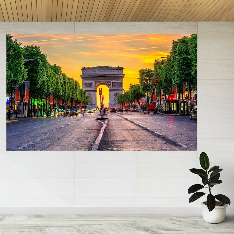 May include: A sunset view of the Arc de Triomphe in Paris, France. The iconic monument is surrounded by trees and a street lined with cars. The sky is a vibrant orange and yellow.