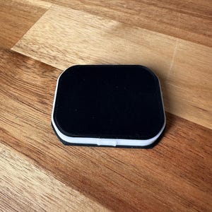 Puede incluir: Un objeto cuadrado negro con un borde blanco, sentado sobre una superficie de madera.