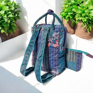 May include: A patterned backpack and matching pouch in teal, blue, and pink. The backpack has adjustable straps, a top handle, and a zip closure. The pouch has a zip and a similar design. The backpack is approximately 36 cm tall.