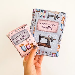 May include: Two needle cases, one pink and one blue, with a sewing machine and thread design. The pink case says "Hand Sewing Needles" and the blue case says "Sewing Machine Needles".