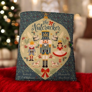 May include: A teal book cover with a festive design from "The Nutcracker". The central oval design features a nutcracker, mouse king, and ballerina. The words "The Nutcracker" are written across the top. The cover is decorated with festive elements.