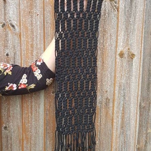 May include: Black macrame wall hanging with a wooden dowel at the top and long fringe at the bottom.