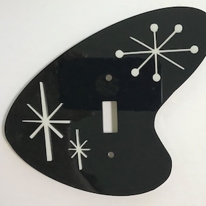 May include: Black light switch cover with a white starburst design. The cover is shaped like a boomerang.