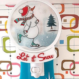 May include: A decorative night light featuring a snowman skating in a snow globe. The snowman wears a red hat and scarf, and the base is blue. The words "Let it Snow" are in red script.