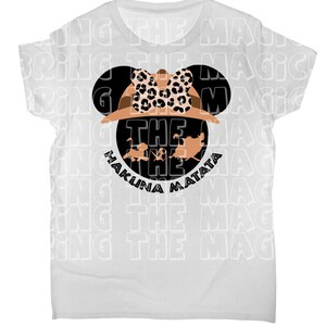 Op de afbeelding: Wit T-shirt met een zwart en bruin Mickey Mouse-hoofd ontwerp. Het Mickey Mouse-hoofd draagt een safarihoed met een luipaardprint strik. De tekst "Hakuna Matata" en "The" zijn in zwart onder het Mickey Mouse-hoofd gedrukt.