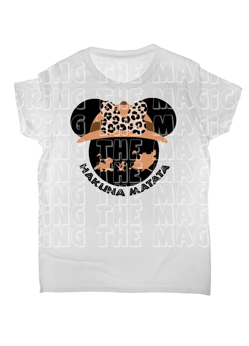 Op de afbeelding: Wit T-shirt met een zwart en bruin Mickey Mouse-hoofd ontwerp. Het Mickey Mouse-hoofd draagt een safarihoed met een luipaardprint strik. De tekst "Hakuna Matata" en "The" zijn in zwart onder het Mickey Mouse-hoofd gedrukt.