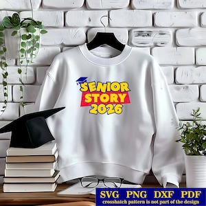 May include: White sweatshirt with the text "SENIOR STORY 2026" in yellow, red, and blue. A graduation cap is above the text. A black graduation cap and a stack of books are in the foreground.
