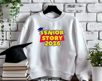 May include: White sweatshirt with the text "SENIOR STORY 2026" in yellow, red, and blue. A graduation cap is above the text. A black graduation cap and a stack of books are in the foreground.