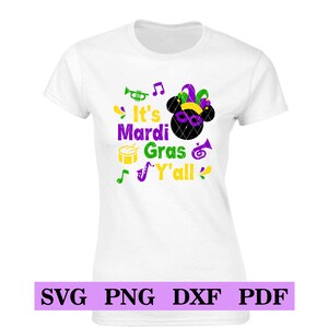 May include: White t-shirt with a purple, green and yellow design. The design features a cartoon mouse head with a jester's hat, musical notes, a trumpet, a drum and a saxophone. The text reads "It's Mardi Gras Y'all".