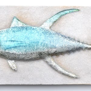 May include: A ceramic sculpture of a tuna fish, painted in shades of blue and silver, on a white background. The fish is depicted realistically with detailed scales and fins. The artist's initials, "C.W.", are signed in the bottom right corner.