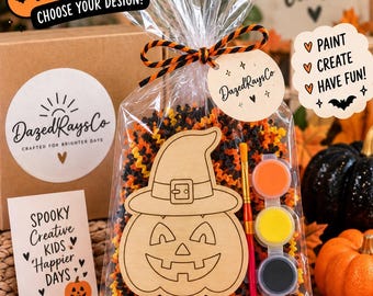 Può includere: Un kit di pittura fai-da-te per Halloween in un sacchetto di plastica trasparente contenente una sagoma di zucca in legno con cappello da strega, un pennello e tre piccoli vasetti di vernice arancione, gialla e nera, riempito con materiale arancione e nero.