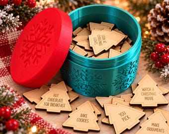 Può includere: Un contenitore rotondo color verde acqua con un coperchio rosso decorato con un fiocco di neve, riempito con gettoni di legno a forma di albero di Natale. Ogni gettone riporta incise attività natalizie come "Look at Christmas lights" e "Bake cookies".
