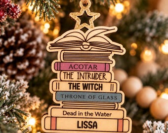 Può includere: Un ornamento in legno a forma di pila di libri sormontata da una stella. I dorsi dei libri riportano le scritte ACOTAR, THE INTRUDER, THE WITCH, THRONE OF GLASS, Dead in the Water e LISSA. L'ornamento è appeso a un cordino di juta.