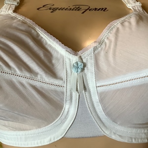 May include: White bra with a delicate floral design and a centre bow. The bra has a sheer mesh fabric and a delicate lace trim. The bra is labelled "Exquisite Form".