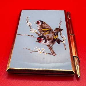 May include: A vintage gold-toned pen and a matching case. The case features a light blue background with a detailed illustration of two birds perched on a flowering branch. The birds have brown, black, and yellow feathers.