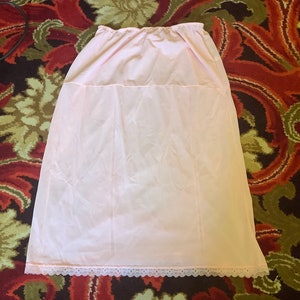 May include: A pale pink slip skirt with a lace trim. The skirt is laying flat on a patterned rug.