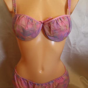 May include: A pink and purple floral print bra and panty set. The bra has a sweetheart neckline and adjustable straps. The panty has a low rise and a full coverage back.