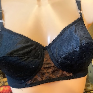 Puede incluir: Sujetador de encaje negro con textura satinada y tirantes ajustables. El sujetador tiene un delicado patrón floral y una copa lisa y sin costuras.