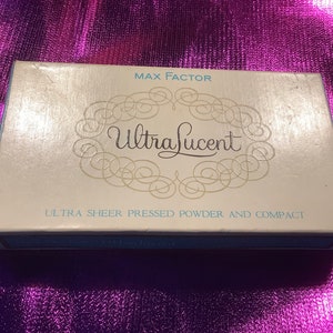 Può includere: Una scatola bianca con un bordo blu e il testo "MAX FACTOR UltraLucent ULTRA SHEER PRESSED POWDER AND COMPACT" stampato su di essa.