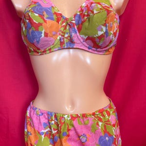 May include: A floral print bra and matching shorts set. The bra has adjustable straps and a front tie. The shorts have an elastic waistband. The print features pink, orange, purple, and green flowers on a white background.