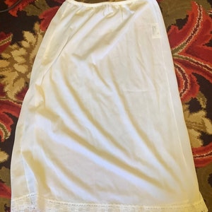 May include: White slip skirt with a lace trim. The skirt is made of a lightweight fabric and has a simple, classic design.