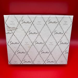 May include: A white box with a repeating pattern of the word "Stratton" and the text "Made in England" in a diamond grid. The box is on a red background.