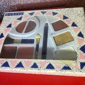 Könnte beinhalten: Eine weiße Make-up-Palette mit einem geometrischen Muster in Rosa und Blau. Die Palette enthält Lidschatten, Rouge, einen Pinsel und einen Eyeliner. Der Markenname "evelte" ist auf der Vorderseite der Palette aufgedruckt.