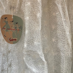 May include: White sheer fabric with a delicate floral pattern and a small tag that reads "but...underneath it all...Sidroy".