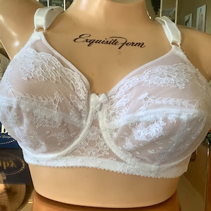 May include: White lace bra with adjustable straps and a bow detail in the center. The bra is on a white mannequin. The text "Exquisite Form" is printed on the mannequin's chest.