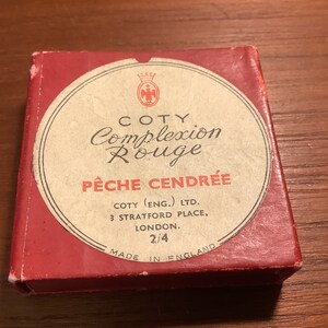 May include: A red box with a white circle containing the text "COTY Complexion Rouge PÊCHE CENDRÉE" and the text "COTY (ENG.) LTD. 3 STRATFORD PLACE, LONDON. 2/4 MADE IN ENGLAND".