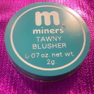 Könnte beinhalten: Ein runder, türkisfarbener Kompakt mit dem Text "m miners TAWNY BLUSHER 0.07 oz. net wt. 2g."