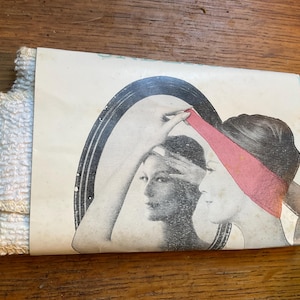Puede incluir: Un paquete vintage de toallitas blancas. El embalaje presenta una ilustración retro de una mujer mirándose en un espejo, con una cinta roja en la cabeza. Las toallitas están dobladas y apiladas.