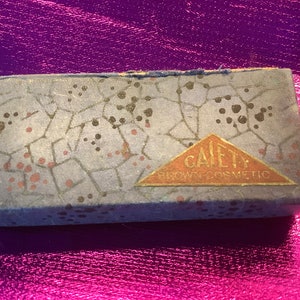 Könnte beinhalten: Eine vintage blaue und weiße Schachtel mit einem roten und goldenen Dreiecksaufkleber mit der Aufschrift "Gaiety Brow Cosmetic".