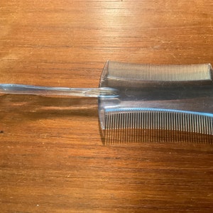 May include: A clear plastic comb with a handle and fine teeth. The comb is designed for detangling hair.