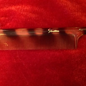 May include: A brown and black tortoise shell comb with the word "Stratton" printed on the handle.