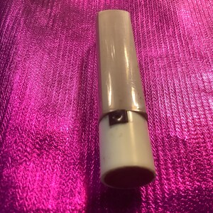Può includere: Un tubetto di rossetto bianco con una fascia argentata al centro.