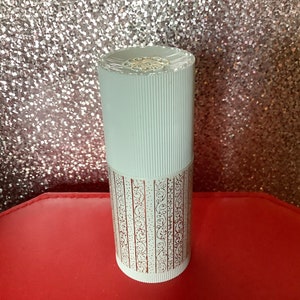 Könnte beinhalten: Weiße zylindrische Flasche mit einem goldenen und weißen Muster. Die Flasche hat einen weißen Verschluss mit einem goldenen Design.