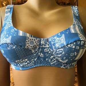 May include: A blue and white patchwork-patterned bra with wide straps. The bra features a variety of floral and geometric designs in white against a blue background. The bra is displayed on a mannequin.