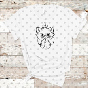 May include: White t-shirt with a black and white outline of a cartoon cat with a bow on its head. The cat is wearing a bow tie and has its paws clasped together. The t-shirt has a white background with small black polka dots.
