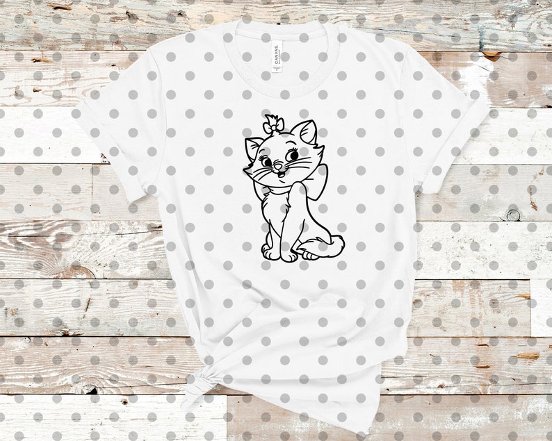 May include: White t-shirt featuring a black and white illustration of a cartoon cat with a bow and a bow on its head. The shirt has a crew neck and short sleeves. The background is a light gray polka dot pattern.