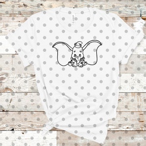 May include: White t-shirt with a black and white outline of Dumbo the elephant with big ears. The shirt has a white background with small gray polka dots.