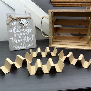 May include: A wooden crate with a sign that reads "There is always something to be thankful for". The crate is sitting on a table with two brown cardboard dividers.