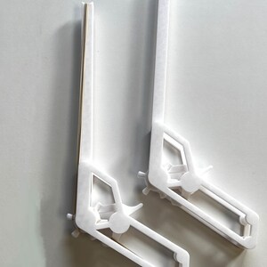 May include: Two white plastic bookends shaped like a construction vehicle. The bookends are angled and have a cutout design of a vehicle with wheels.