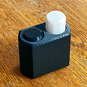 May include: A black plastic holder with two round buttons, one black and one white. The holder is on a wooden surface.