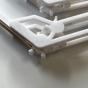 May include: White plastic clips with a gold metal spring. The clips are designed to hold items together.