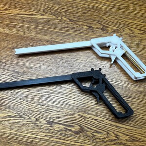 May include: Two toy guns, one black and one white, are lying on a wooden surface. The guns are made of plastic and have a simple design.