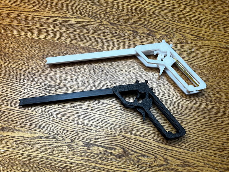 May include: Two toy guns, one black and one white, are lying on a wooden surface. The guns are made of plastic and have a simple design.