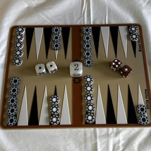 May include: A brown backgammon board with white and black triangles. There are white and brown dice on the board. The board has the words "Black Home" and "White Home" printed on it.