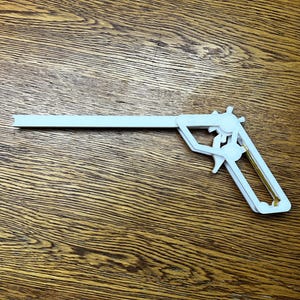May include: A white plastic toy gun with a gold trigger. The gun is shaped like a pistol and has a long barrel.