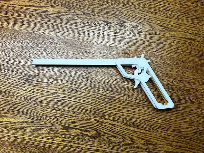 May include: A white plastic toy gun with a gold trigger. The gun is shaped like a pistol and has a long barrel.